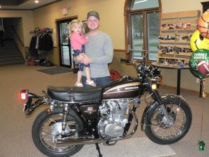 The mastermind behind the project, Jonny Rankin, holds daughter Charlie in front of the restored motorcycle at the reveal party.